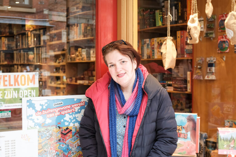 Kim Hoetjes staat voor haar spelletjeswinkel Wir War in de Oude Kijk in ’t Jatstraat, omringd door kleurrijke spellen en posters.