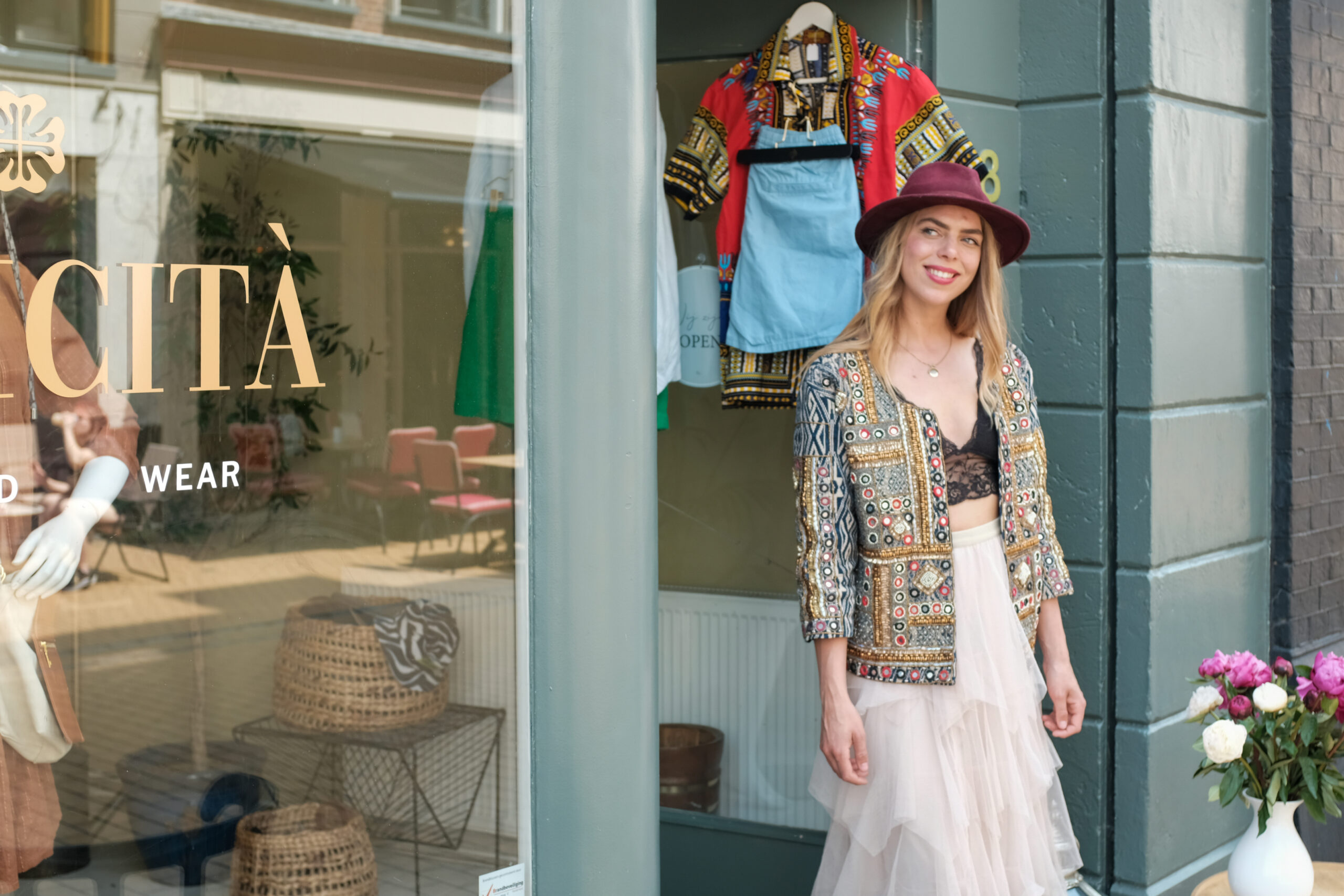 Vrouw in kleurrijke tweedehands bohemian outfit voor de etalage van tweedehands kledingboetiek Felicità aan de Zwanestraat in Groningen