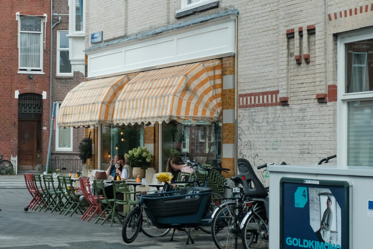 Terras van café Struis aan de Kraneweg in de Schildersbuurt, met fietsen en gekleurde stoelen.