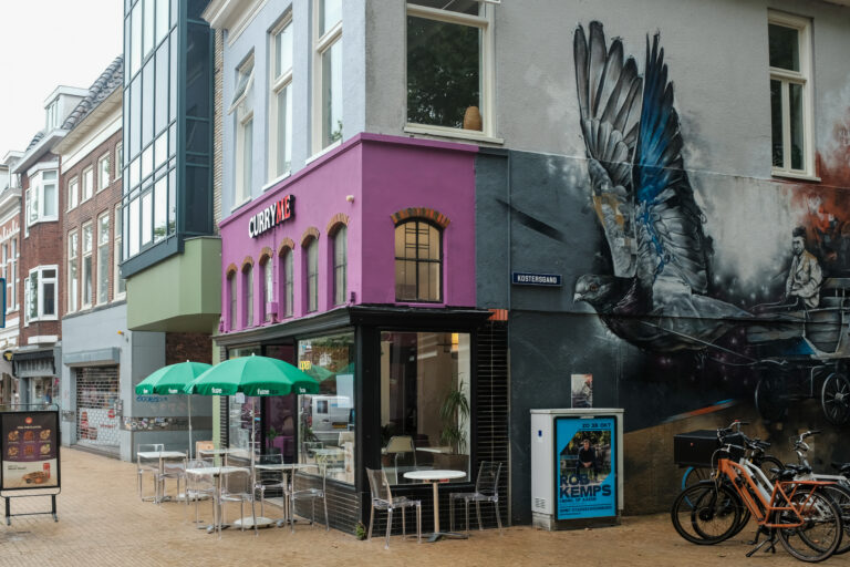 Vooraanzicht van restaurant Curry Me aan de Rademarkt 10 in Groningen, met kleurrijke gevel, buitenterras en opvallende muurschildering